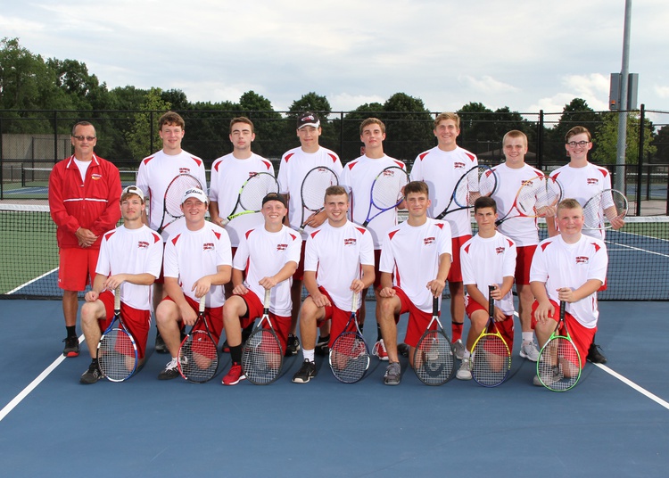  The Varsity and Junior Varsity members posing with their coach in front of the tennis      court's net